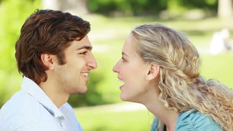 a couple look at each other as they kiss in the park and then look at the camera