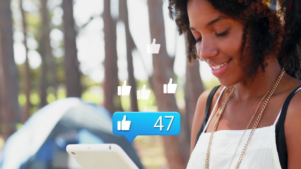 Woman holding tablet in forest campground, displaying floating social media notification icons