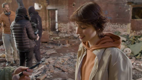 a production worker making up a red haired actress in a ruined building