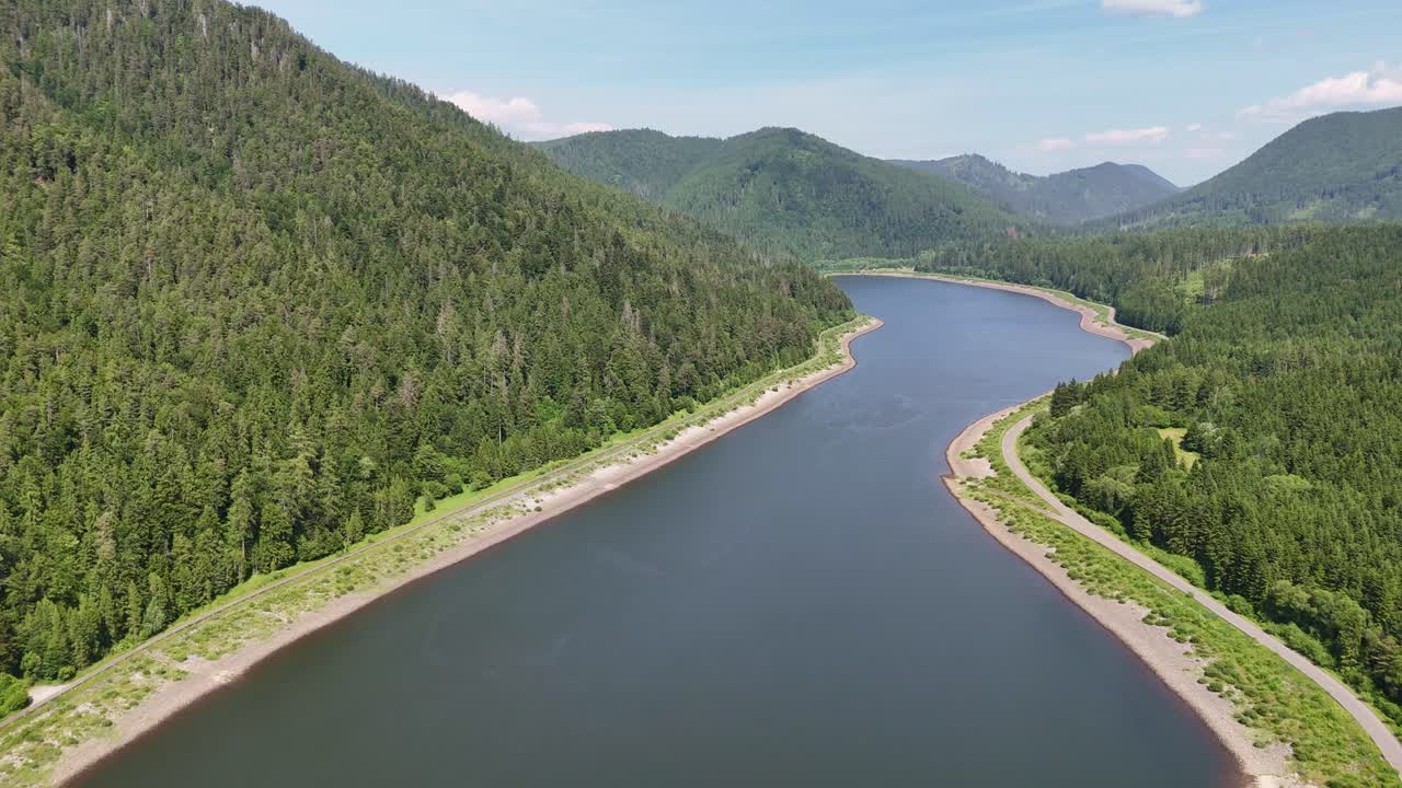 Drone flying backward and ascending above Čierny Váh dam, revealing the wide reservoir, forested mountains, and scenic Slovak landscape in summer