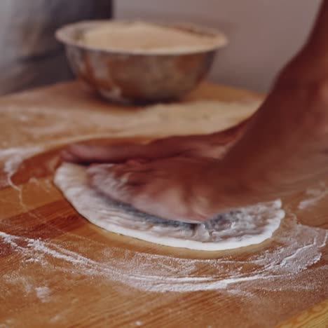 baker kneading dough in flour on table. hands of professional bakery chef on dough. man forming dough of a round form for pizza.