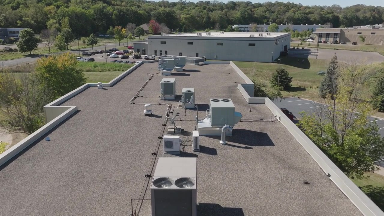 Drone footage of HVAC units on the roof of a commercial building, showcasing industrial systems and architectural design from an elevated perspective under clear skies.