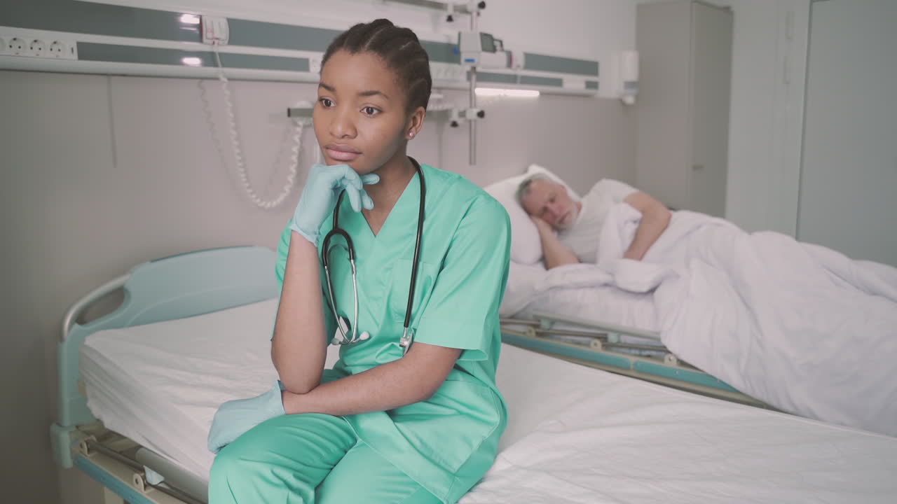A Beautiful Young American Nurse Sitting On The Edge Of A Hospital Bed Thinking