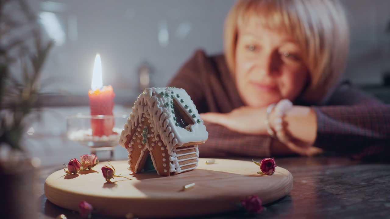 불빛이 그녀의 얼굴을 비추는 나무 트레이에 장식된 케이크를 쳐다보며 테이블에 누워있는 여성, 부드러운 빛과 건조한 꽃으로 따뜻한 분위기