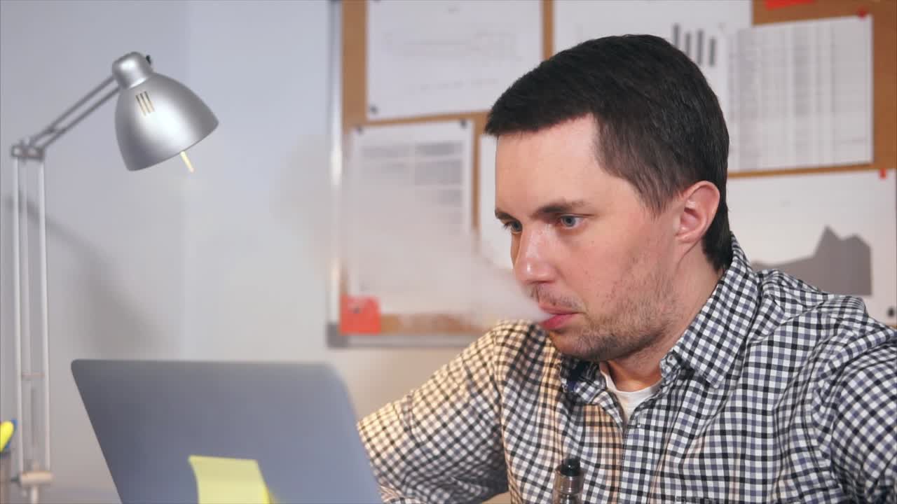 hombre trabajando en una computadora portátil mientras vapea en la oficina