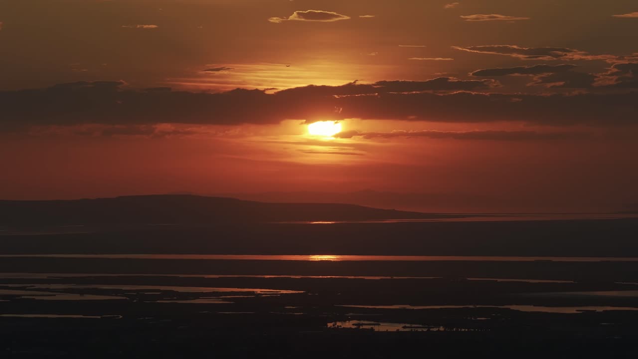 Drone view from Bountiful Canyon in Utah of a golden summer sunset over Salt Lake Valley with clouds, mountains, and water ponds reflecting light from the Great Salt Lake
