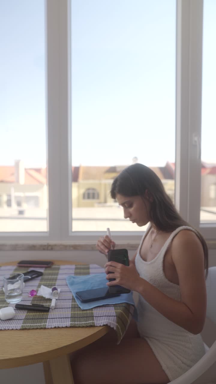 Jovem Mulher Limpando o Smartphone em uma Mesa Perto da Janela