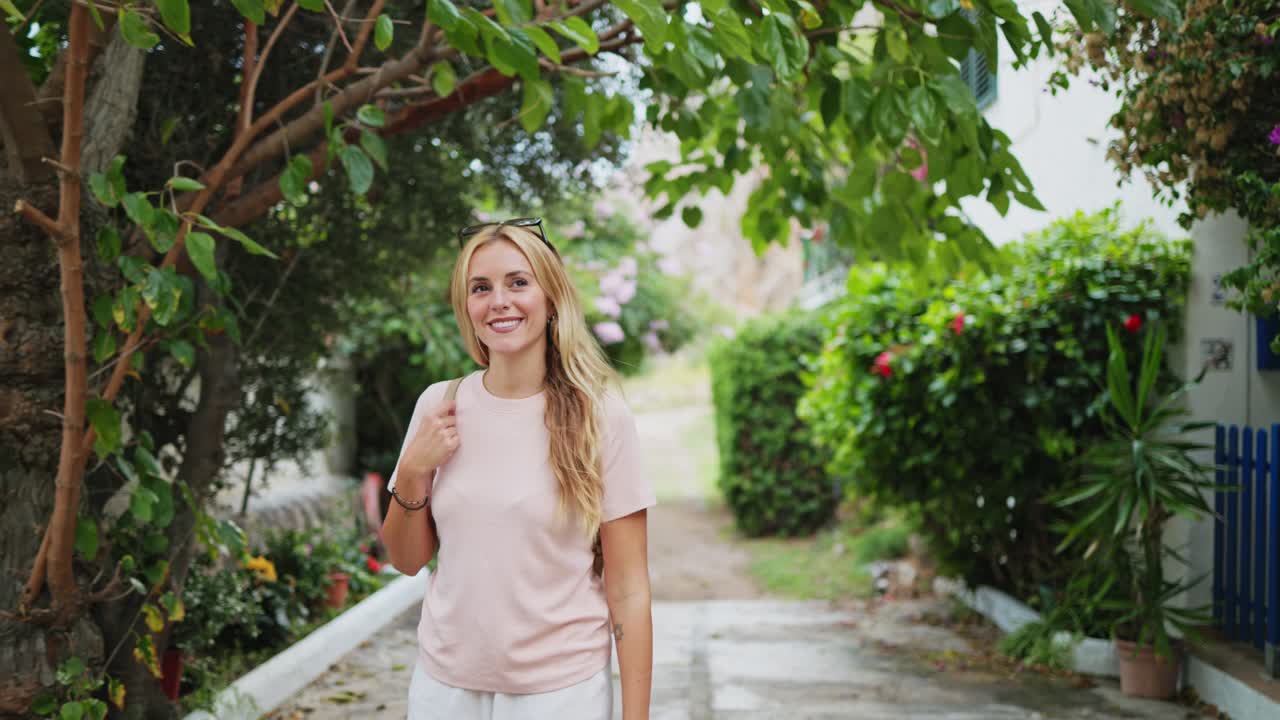 Giovane donna bionda felice che cammina lungo un sentiero di un giardino lussureggiante.