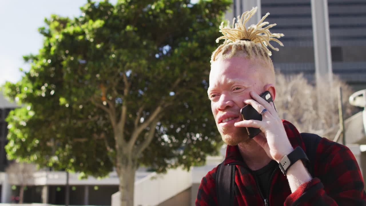 feliz albino hombre afroamericano con rastas en el parque hablando en el teléfono inteligente