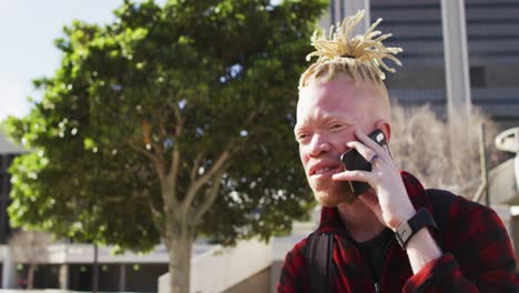 happy albino african american man with dreadlocks in park talking on smartphone