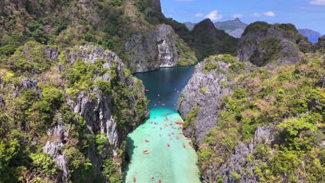 aerial view of big lagoon in miniloc, philippines, with clear turquoise waters, limestone cliffs, lush greenery, and numerous kayakers exploring the tropical paradise under a bright, sunny sky