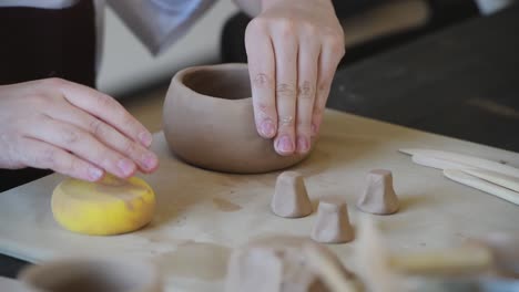 Professional female potter shaping and carving mug with sponge in pottery workshop, studio. Crafting, artwork and handmade concept