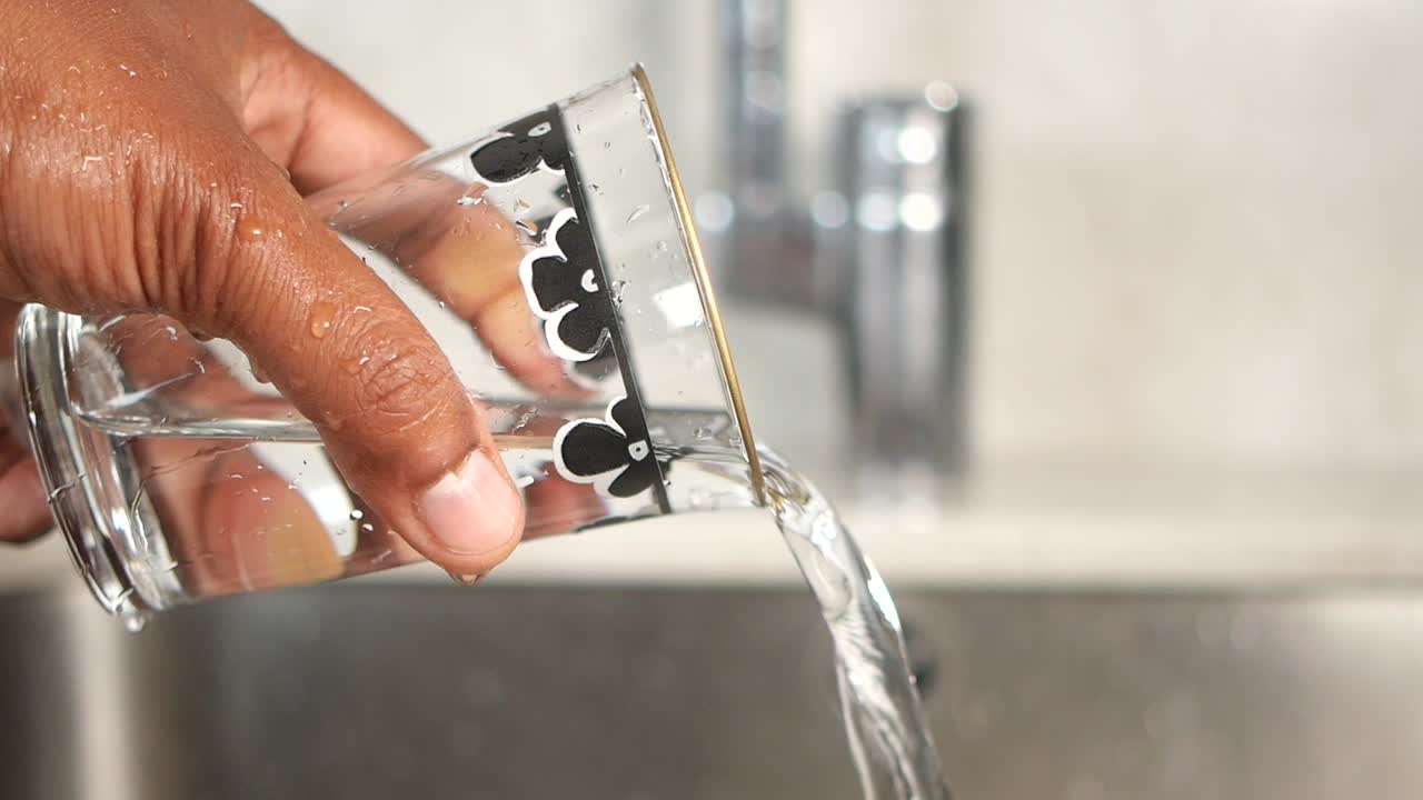 Hand pouring water into a glass at a kitchen sink