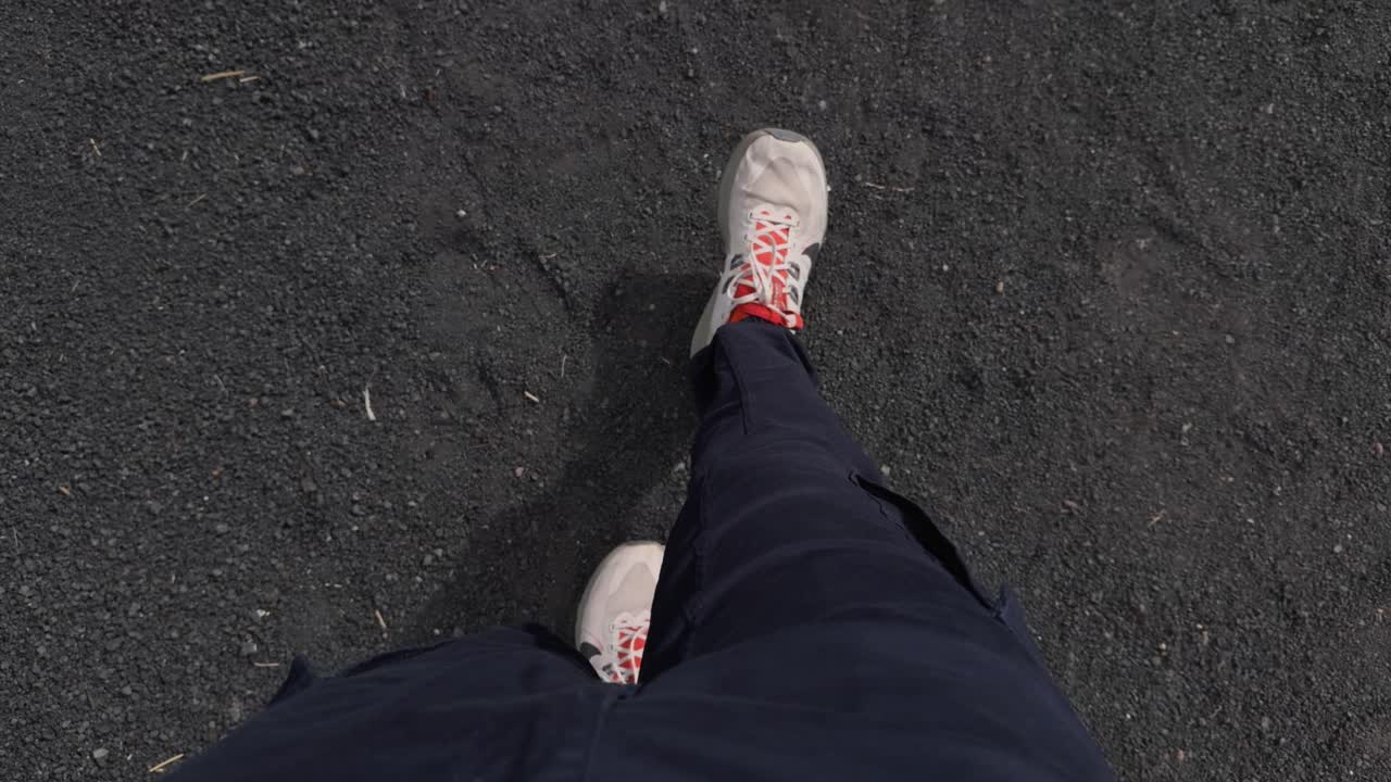 Person's feet wearing sneakers walking on black volcanic sand