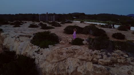woman meditating in yoga position on a cliff overlooking the sea at sunset in ibiza. perfect aerial view flight wide orbit overview drone