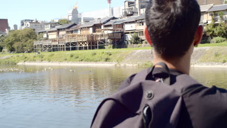 Guy-sitting-alongside-a-river-in-Kyoto,-Japan-soft-lighting