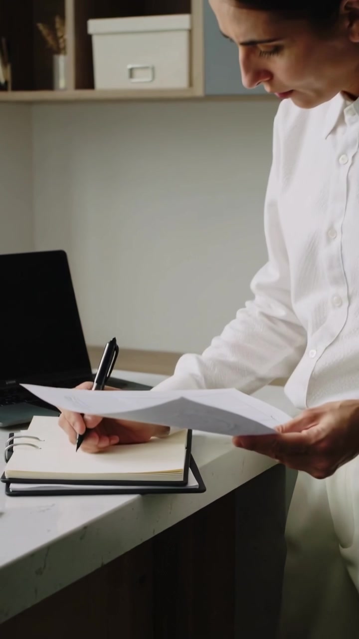 Vídeo vertical: Mulher de blusa branca colocando um documento, copiando uma grade para registrar com uma caneta na mesa para os registros, com espaço para texto.