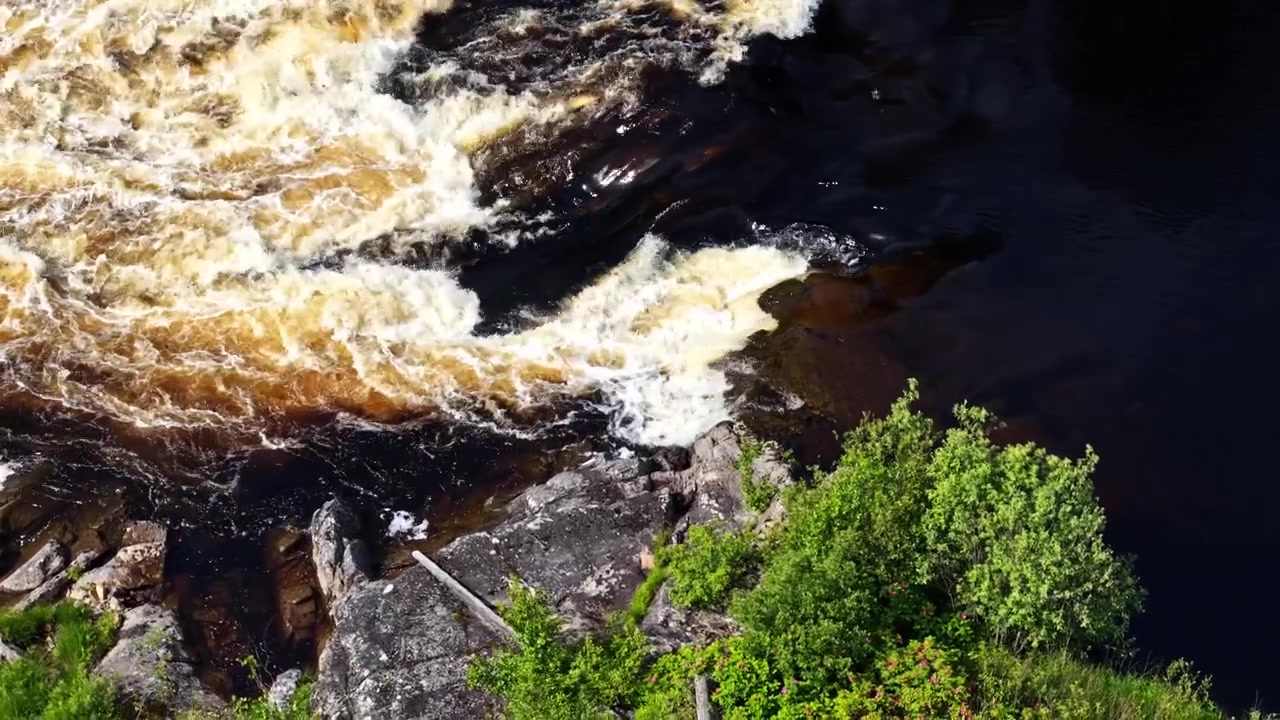 Close aerial of foaming rapids crashing over dark rocks in fast river, drone