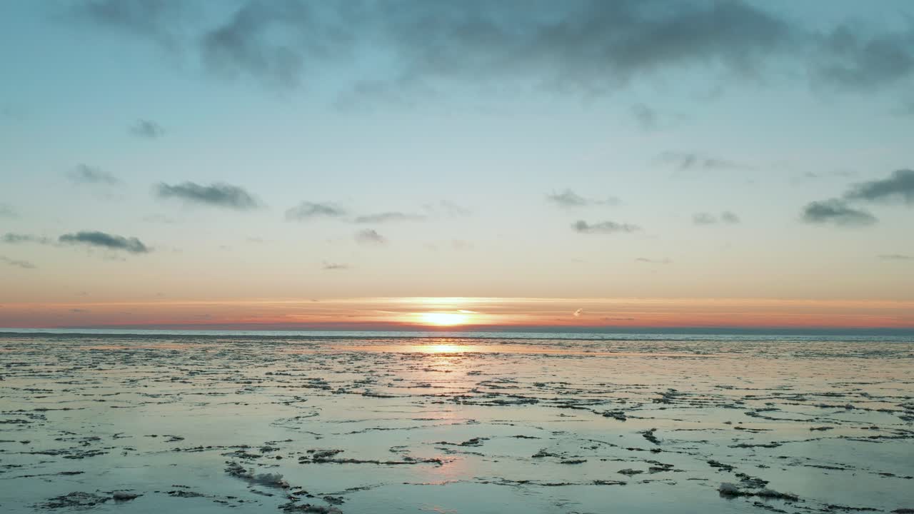 해가 뜰 때 표면에 얼음이 녹은 채 잔잔한 바다 위로 날아가는 드론