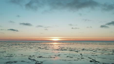 Drone-flying-over-calm-sea-with-melted-ice-at-the-surface-at-sunset,-sunrise