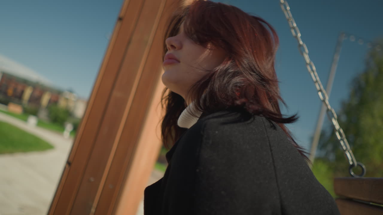 젊은 여자가 웃으며 야외에서 흔들리는 클로즈업, 그녀의 머리카락이 바람에 흔들리는 동안 조정, 밝은 빛 공원에서 활기찬 초록색으로 둘러싸여