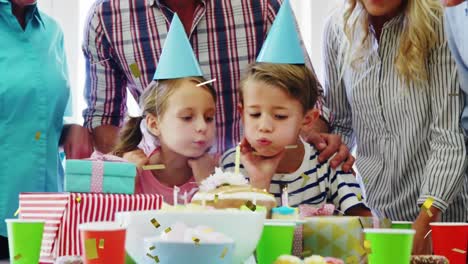 animation of confetti over caucasian boy and girl blowing candles on cake and parents at home