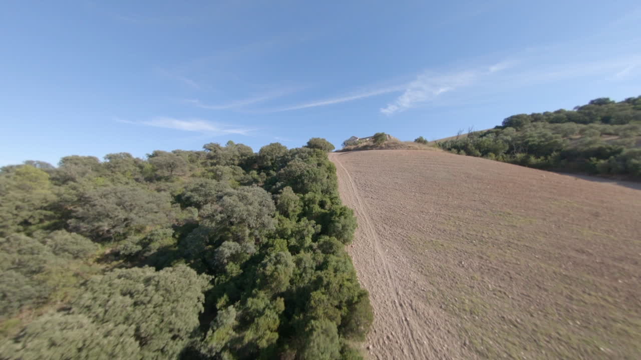 vuelo fpv hasta una cresta boscosa baja cerca de un campo agrícola rocoso seco