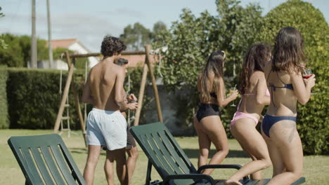 long shot of men and women with cocktails going from the sunbeds to the swimming pool