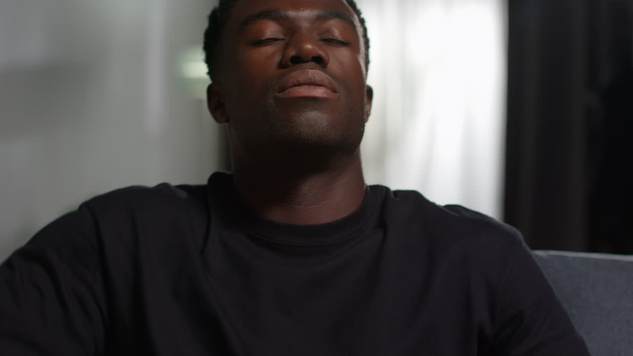 Close Up Of Unhappy And Depressed Young Man Sitting On Sofa At Home Looking Anxious And Worried Rubbing Forehead