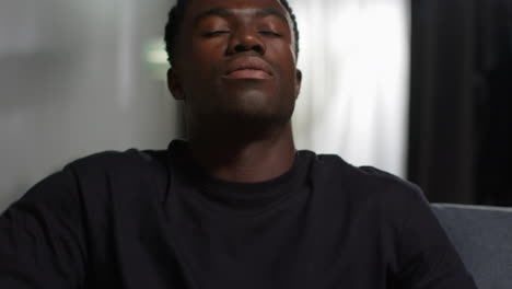 close up of unhappy and depressed young man sitting on sofa at home looking anxious and worried rubbing forehead