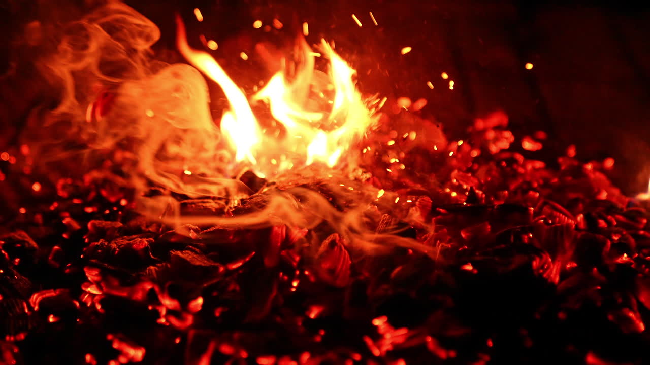 Pushing and poking the embers in the bonfire with a stick. Smoke and sparkles rise up. Close up view.