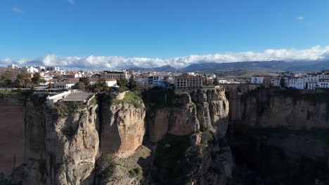 aerial view of ronda, spain, highlighting the stunning puente nuevo bridge on dramatic cliffs, with a picturesque cityscape under a bright blue sky and fluffy clouds