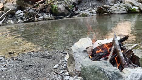 guy adds fire wood to bonfire next to river