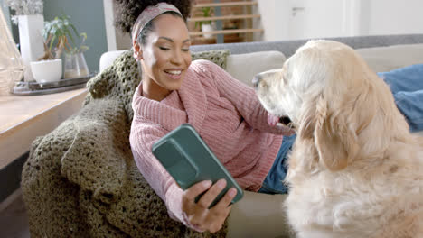mujer biracial feliz tomando una foto con un perro golden retriever usando un teléfono inteligente en casa, en cámara lenta
