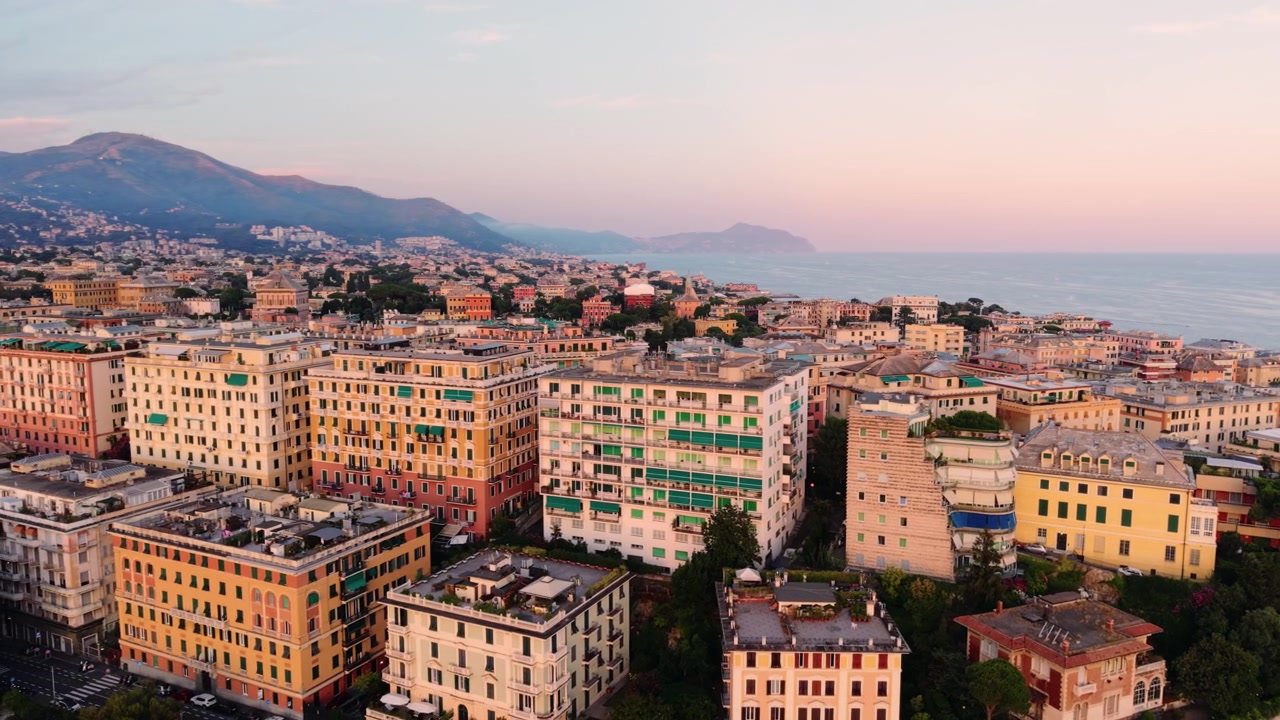 Veduta aerea con panoramica sulla costa di Genova con edifici colorati al tramonto.