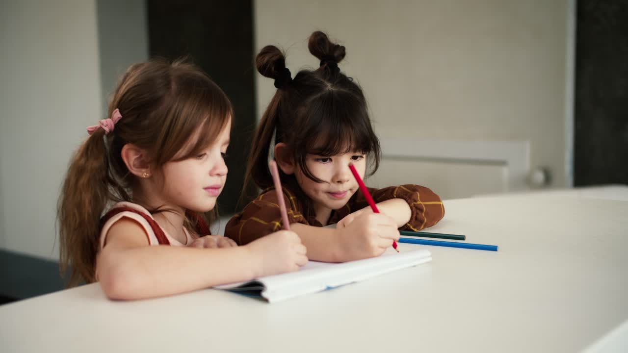 테이블에 있는 두 명의 어린 아이들이 크레이온으로 그림을 그리고 있습니다.