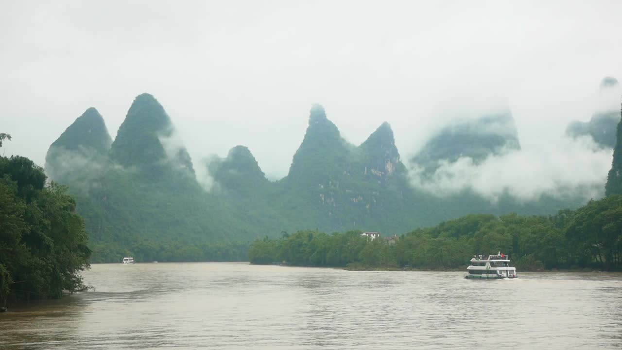 Cruising on a boat along a brown river in Guilin, China. Watching the foggy green mountains in the background