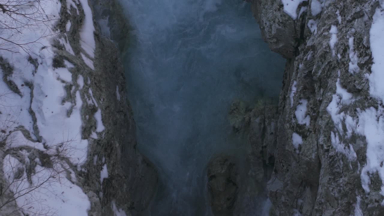 Emerald water of mountain river streaming between frozen rocks covered by snow