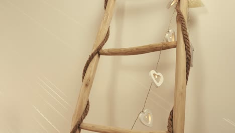 soft, warm shot of a rustic wooden ladder wrapped in rope and delicate heart-shaped string lights, as gentle sun rays dance on the wall, creating a cozy and romantic atmosphere