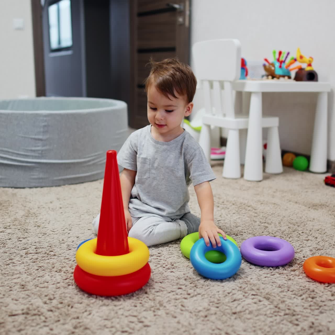 Un bebé adorable sentado en la suave alfombra juega con una pirámide. Un niño feliz se divierte en casa.