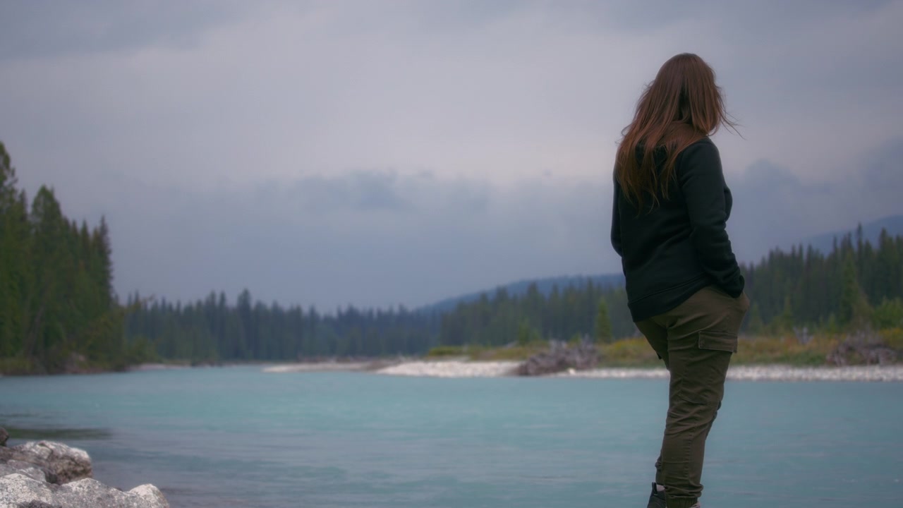 Woman standing near the river shore and looking ahead.
