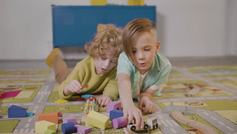 vista frontal de dos niños pequeños jugando con piezas de madera y camión sobre una alfombra en una clase de escuela montessori