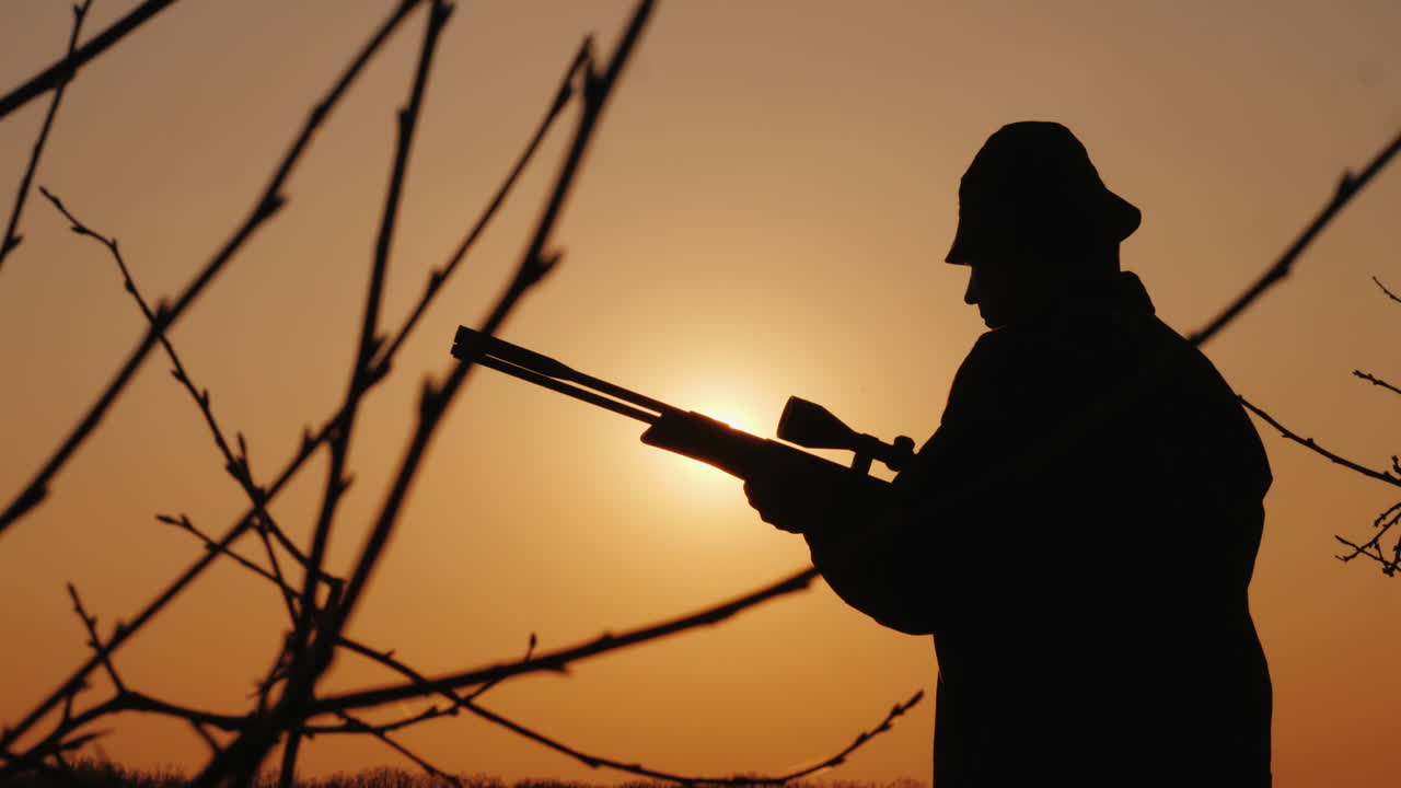 총을 든 사냥꾼의 실루엣 태양 광선이 그의 얼굴에 빛난다