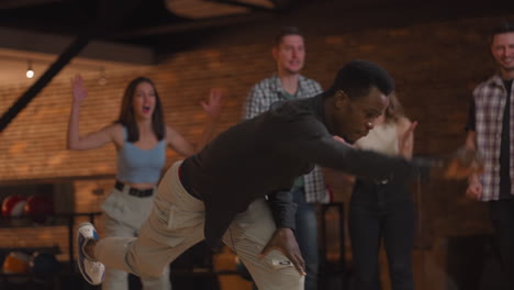 portrait of a black man makes the final throw with a bowling ball and wins the game with the support and joy of his friends of different nationalities. rejoice and celebrate the victory