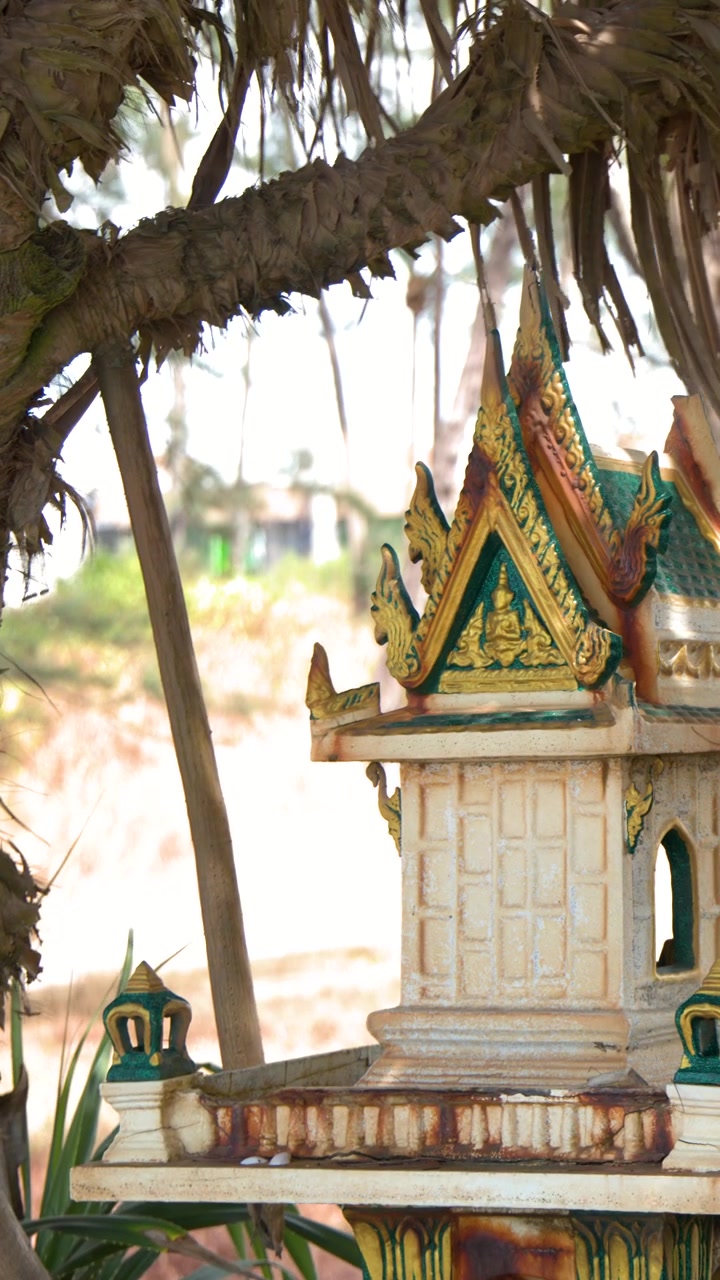 Static medium shot of a miniature Thai spirit house shrine under bright tropical sunlight