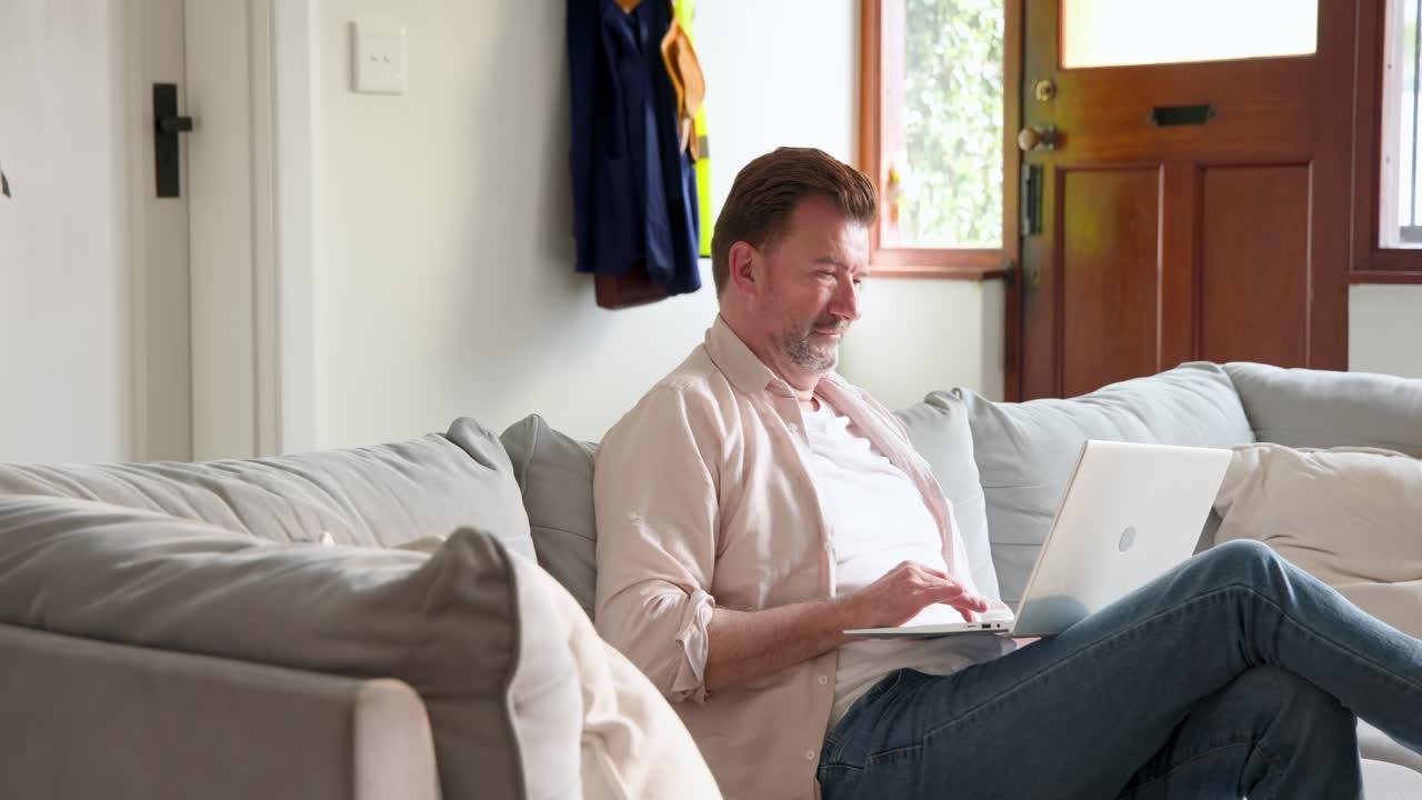 Senior man relaxing on couch using laptop at home, enjoying leisure time