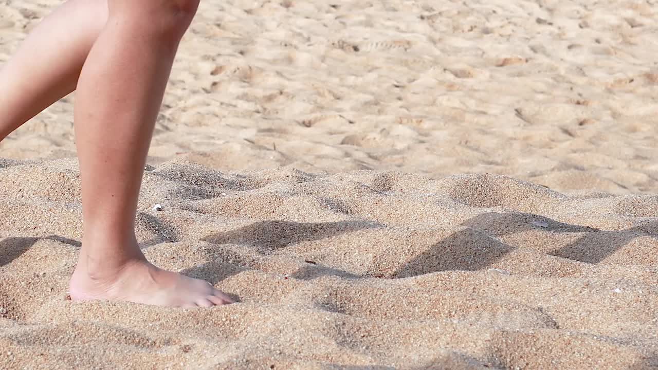 Close-up of bare feet walking on sunlit sandy beach, capturing movement and shadows.