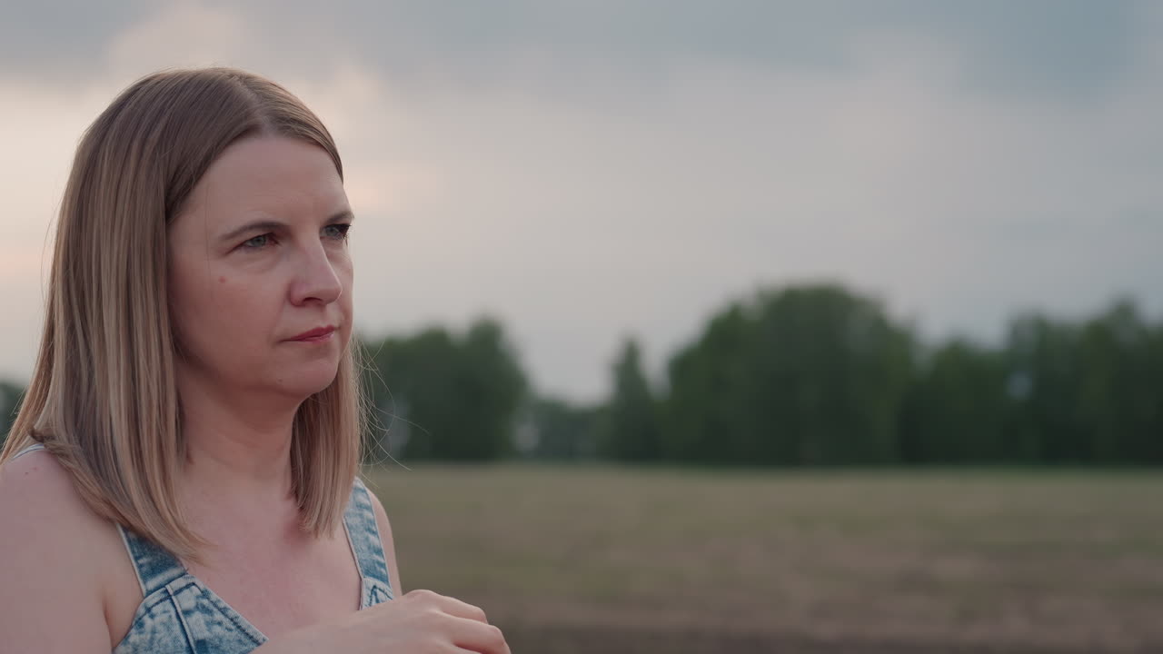 close up of young woman blowing bubbles with plastic wand under pastel sky over expansive farmland capturing serene summer moment and delicate iridescent spheres drifting in gentle breeze
