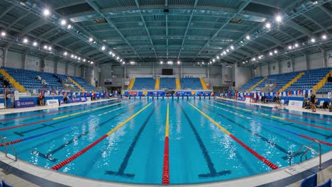 a panoramic view of a modern swimming pool facility showcasing lanes and flags, highlighting the spacious design and aquatic environment for competitive events