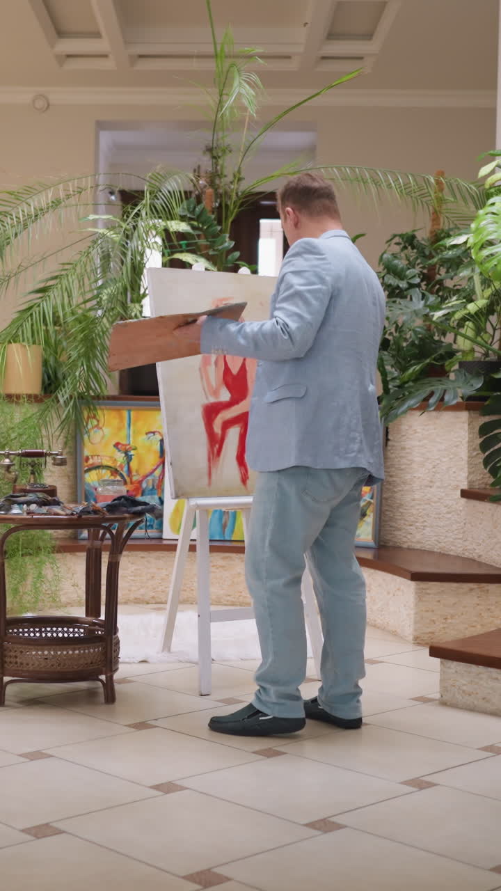 el artista dibuja a una mujer seductora en la mansión. una dama elegante en vestido carmesí se sienta entre las plantas de interior mientras el maestro trabaja en el lienzo. pintura de verdadera belleza